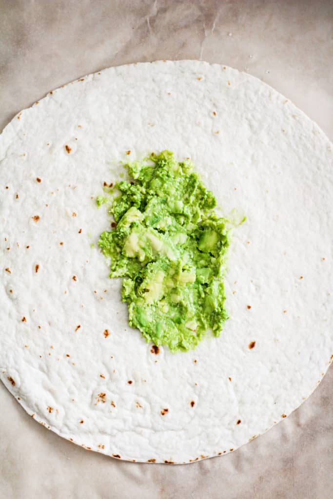 Open tortilla with mashed avocado in the center.