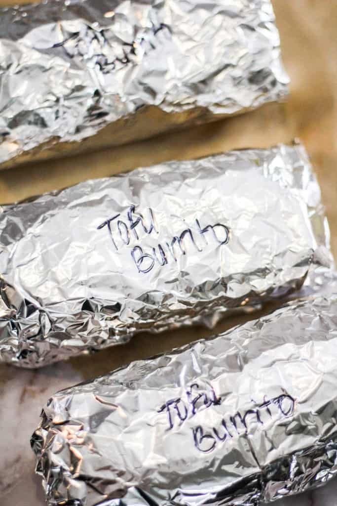 Burritos wrapped in aluminum foil with the label, "tofu burrito" written in black marker.
