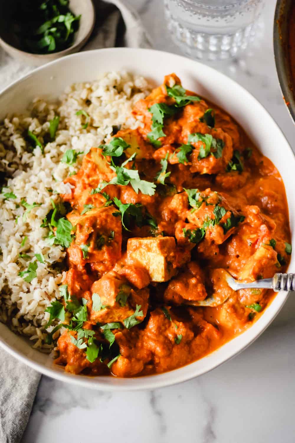 Vertical image of Vegan Tikka Masala with rice and cilantro in a white bowl.