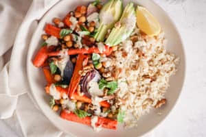Horizontal image of a Vegan Rice Bowl with roasted carrots, chickpeas, avocado, and tahini sauce.
