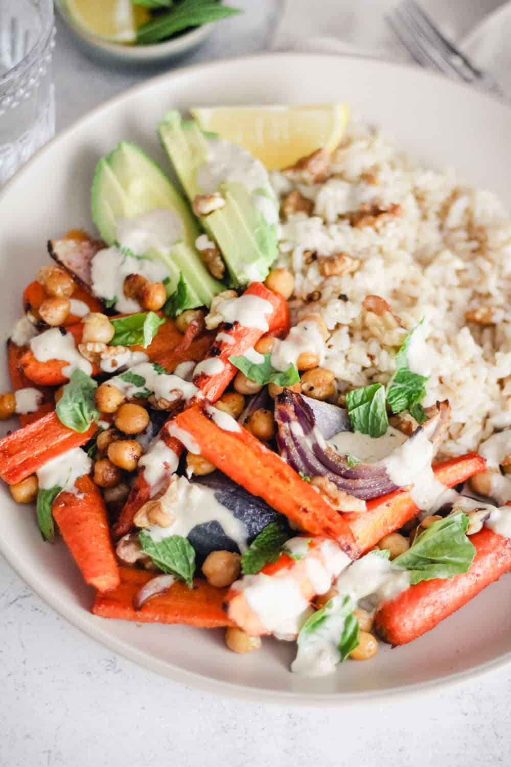 Closeup image of a Vegan Rice Bowl with roasted carrots, onion, chickpeas, and creamy tahini sauce.