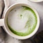 A vanilla matcha latte with frothy oat milk in a white mug.