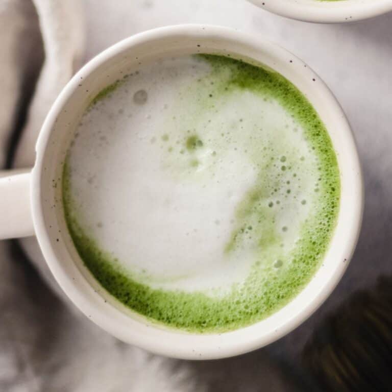 A vanilla matcha latte with frothy oat milk in a white mug.