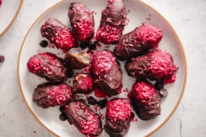 Horizontal image of chocolate covered dates with raspberry topping on a plate.