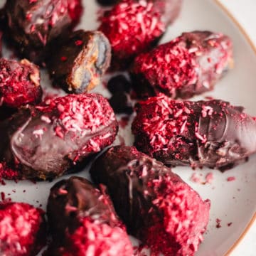 Chocolate covered dates topped with ground raspberries and shredded coconut on a white plate.