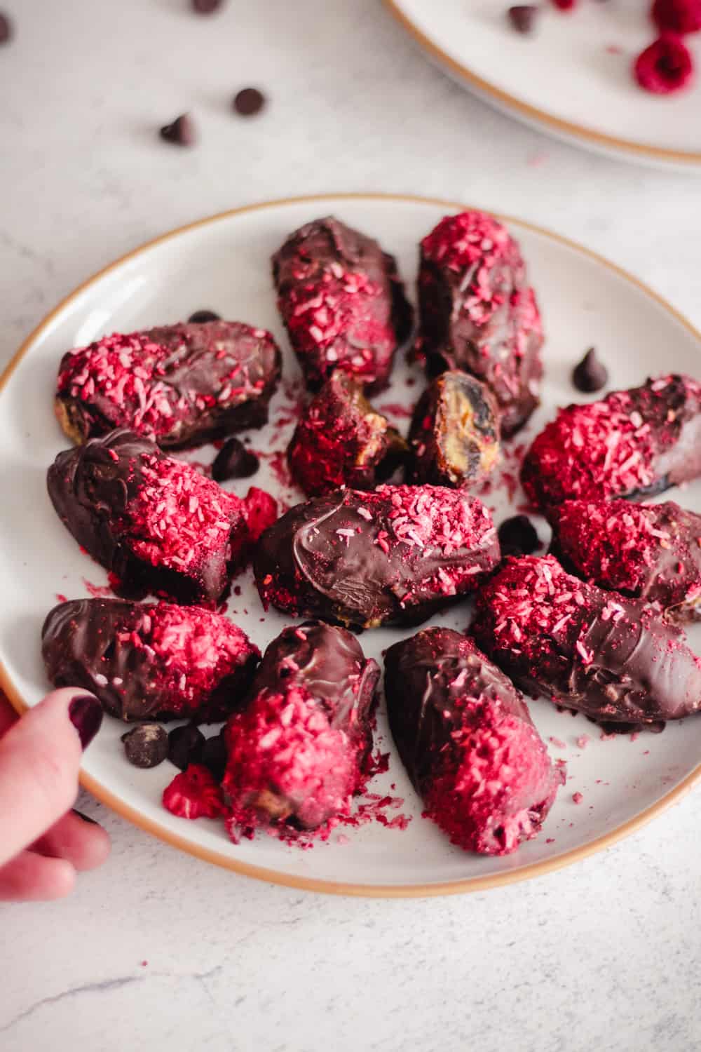 Hand holding a plate of chocolate dates with raspberry topping.