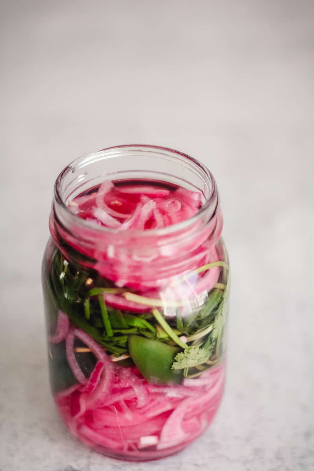 Pickled red onions in a glass jar with jalapeño and herbs.