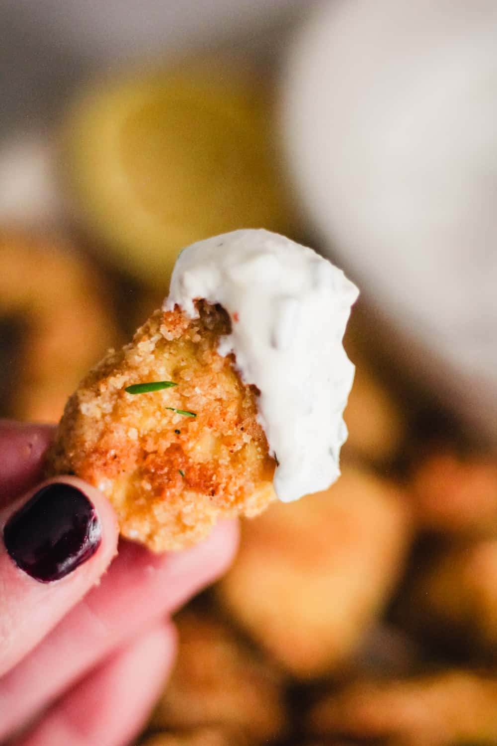 Close-up of a hand holding a crispy tofu nugget dipped in yogurt ranch sauce.
