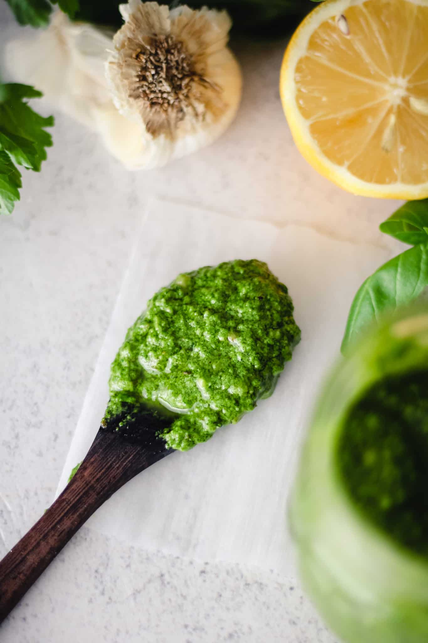 Pesto in a wooden spoon next to lemon, garlic, and basil.