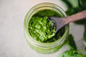 Horizontal overhead image of pesto sauce in a glass jar with a wooden spoon.