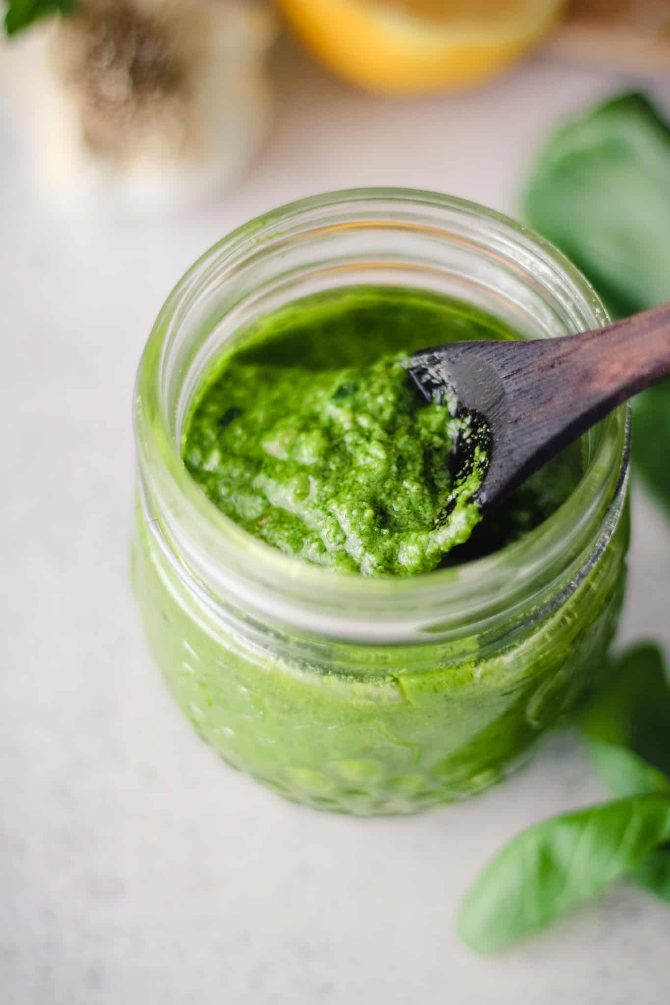 Green pesto sauce in a jar with a wooden spoon.