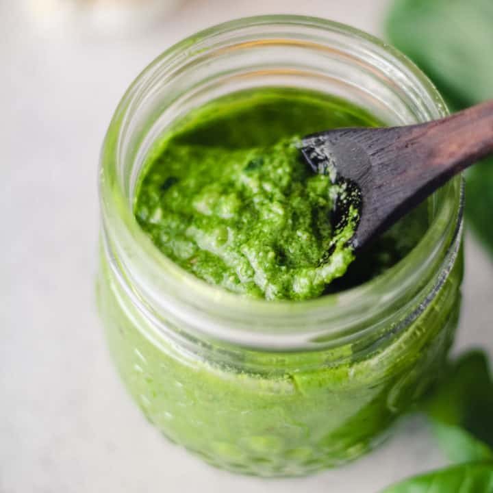 green pesto in a jar with a wooden spoon