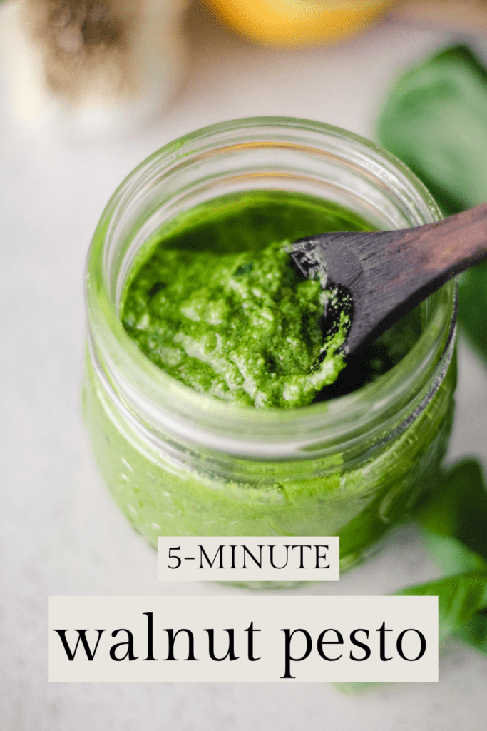 Green pesto sauce in a jar with a wooden spoon. Text reads, "5-Minute Walnut Pesto."