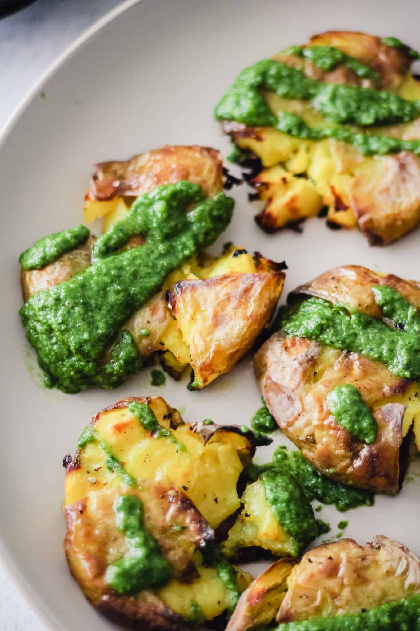 Smashed potatoes covered with pesto sauce on a white plate.