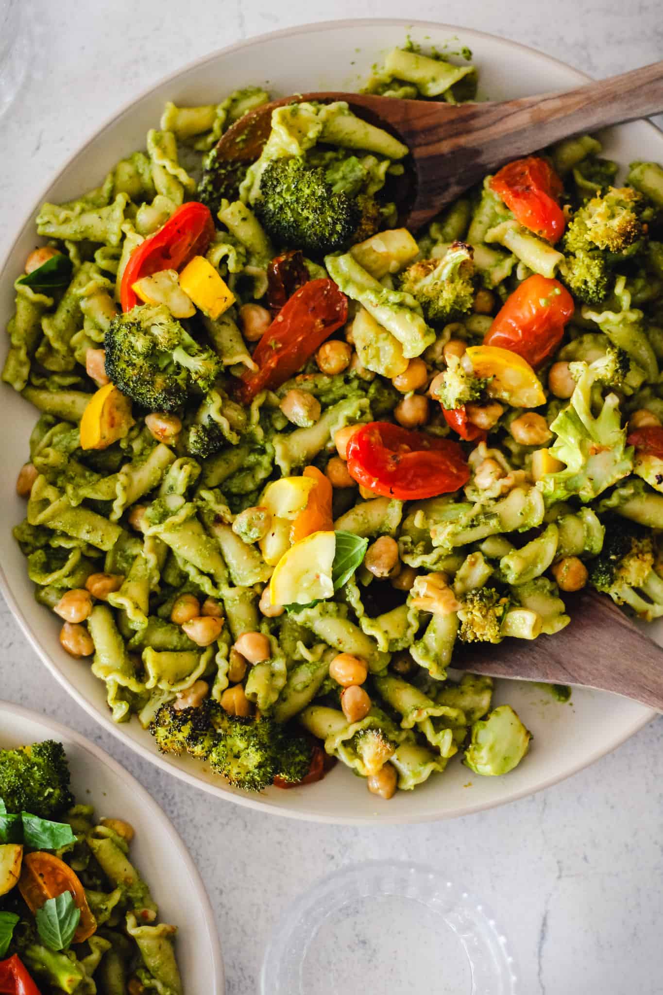 Veggie Pasta Pesto on a cream plate with wooden serving spoons.