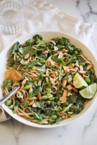 Peanut noodles with edamame, spinach, and lime wedges.