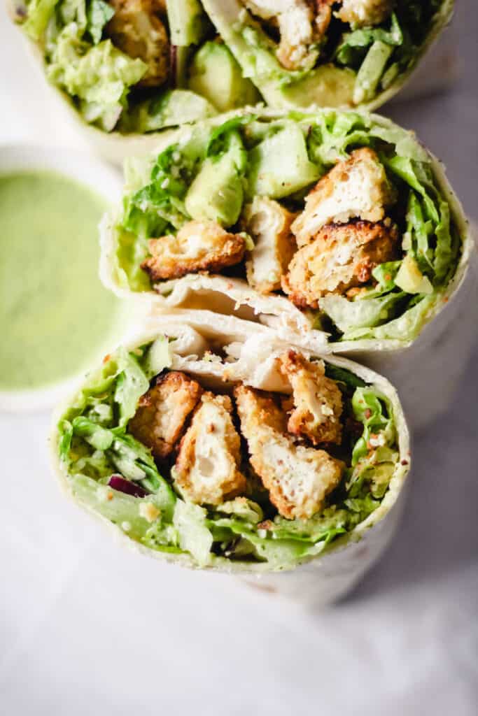 Tofu wrap with lettuce cut in half with a small bowl of green goddess dressing next to it.