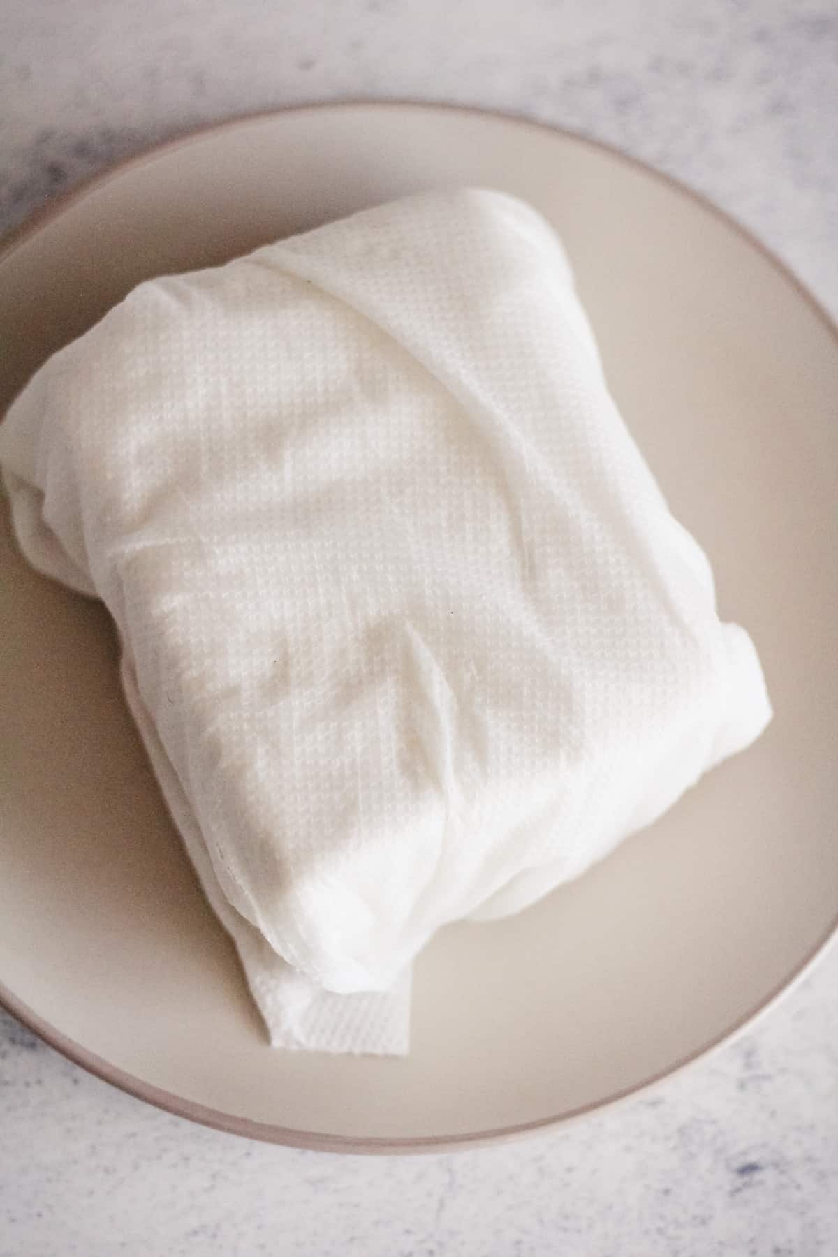 Tofu wrapped in paper towel on a plate.