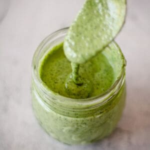 Square image of a spoon coming out of a jar of vegan green goddess dressing.
