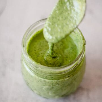 Action shot of a spoon inside a jar of Vegan Green Goddess Dressing.