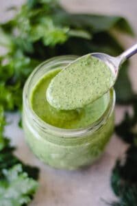 Action shot of a spoonful of green goddess dressing held over the jar.