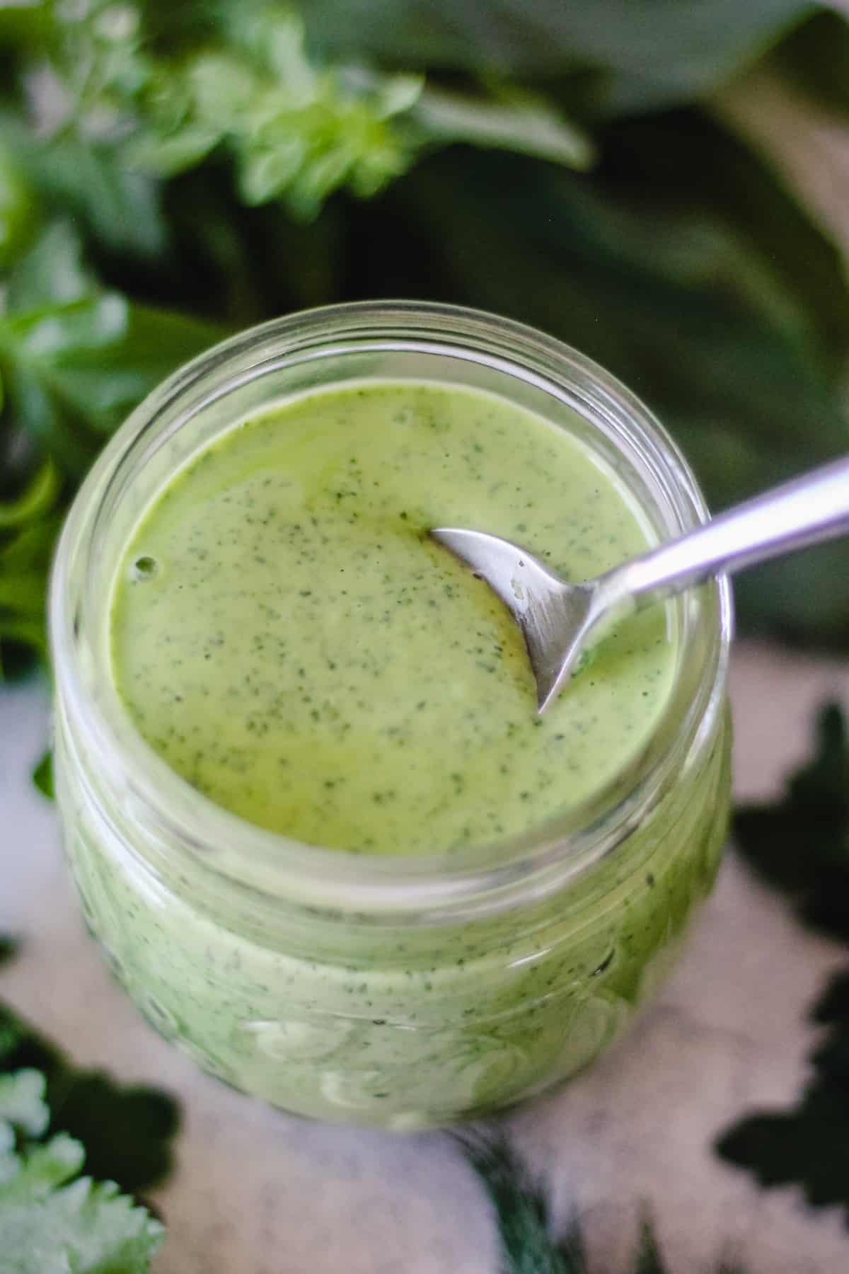 Vegan Green Goddess Dressing in a glass jar surrounded by fresh herbs.