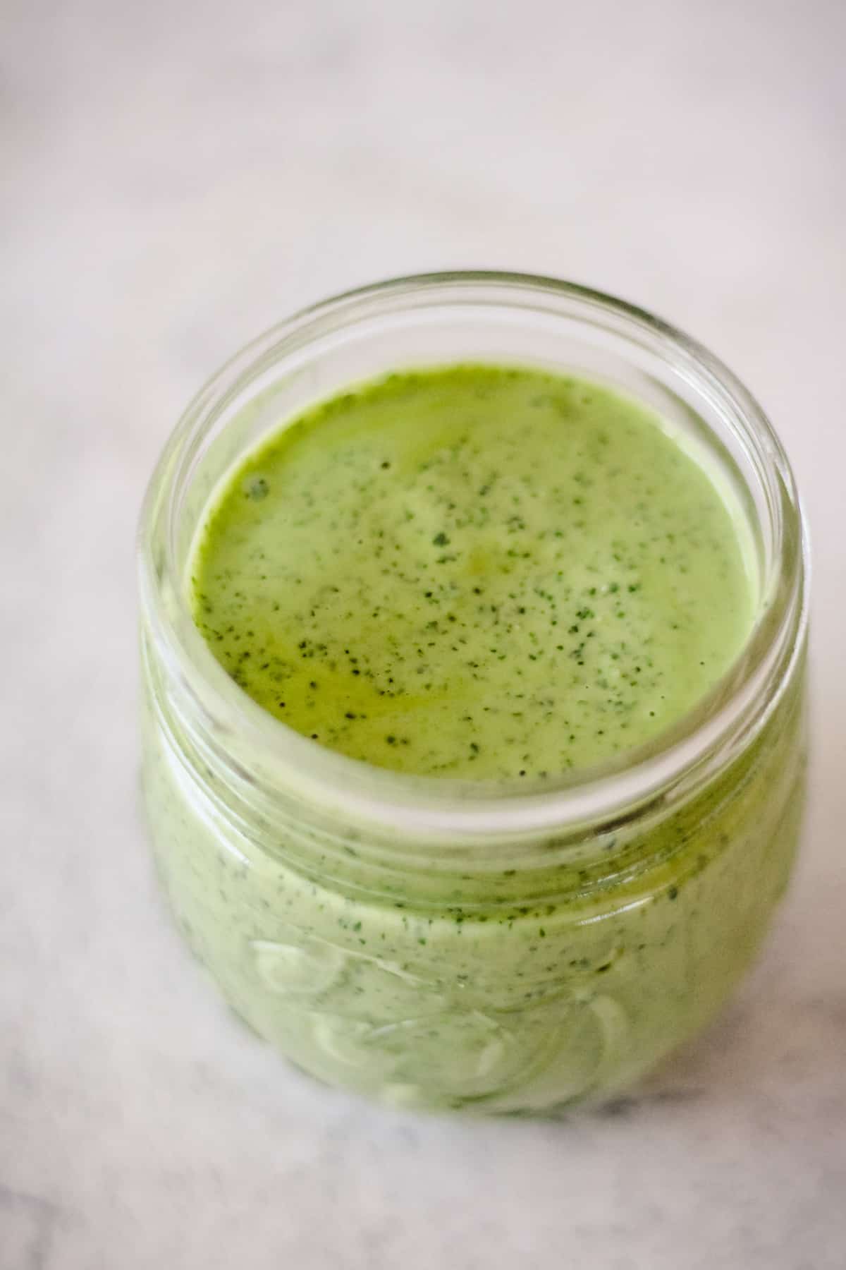 Vegan Green Goddess Dressing in a glass jar with a white background.