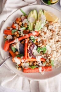 Vegan rice bowl with roasted carrots, avocado, chickpeas, and tahini sauce.