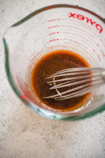 Salad dressing in a liquid measuring cup with a whisk.