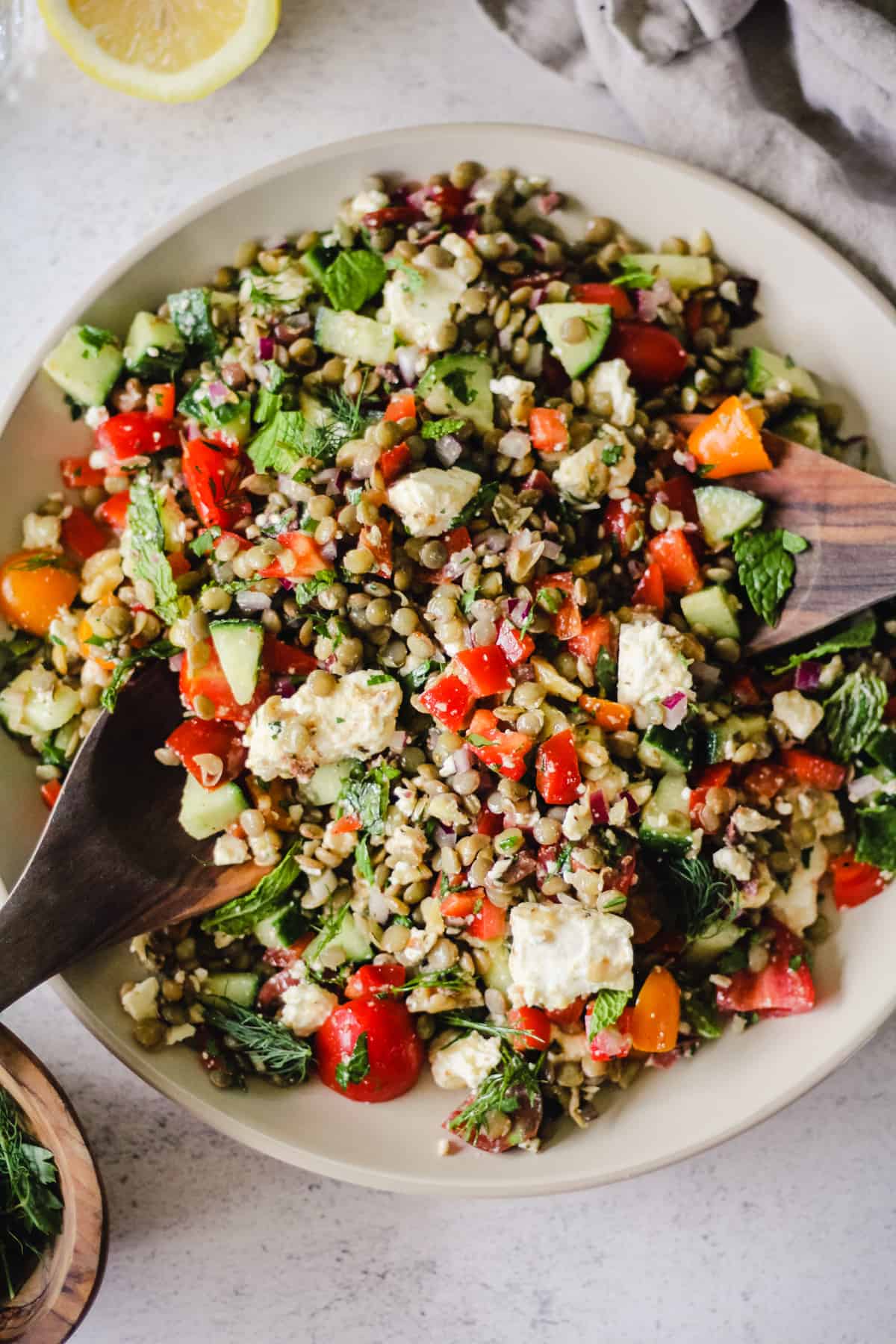 Mediterranean lentil salad on a serving dish with wooden serving spoons.