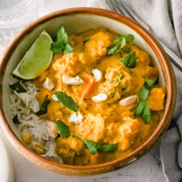 Bowl of creamy pumpkin curry served with rice, lime and fresh herbs.