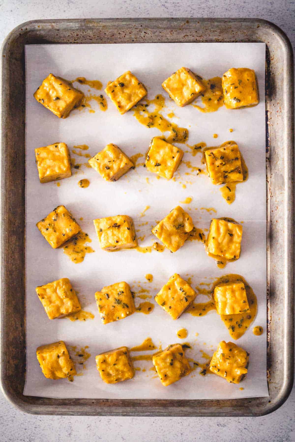 Marinated tempeh cubes spread on a sheet pan before baking.