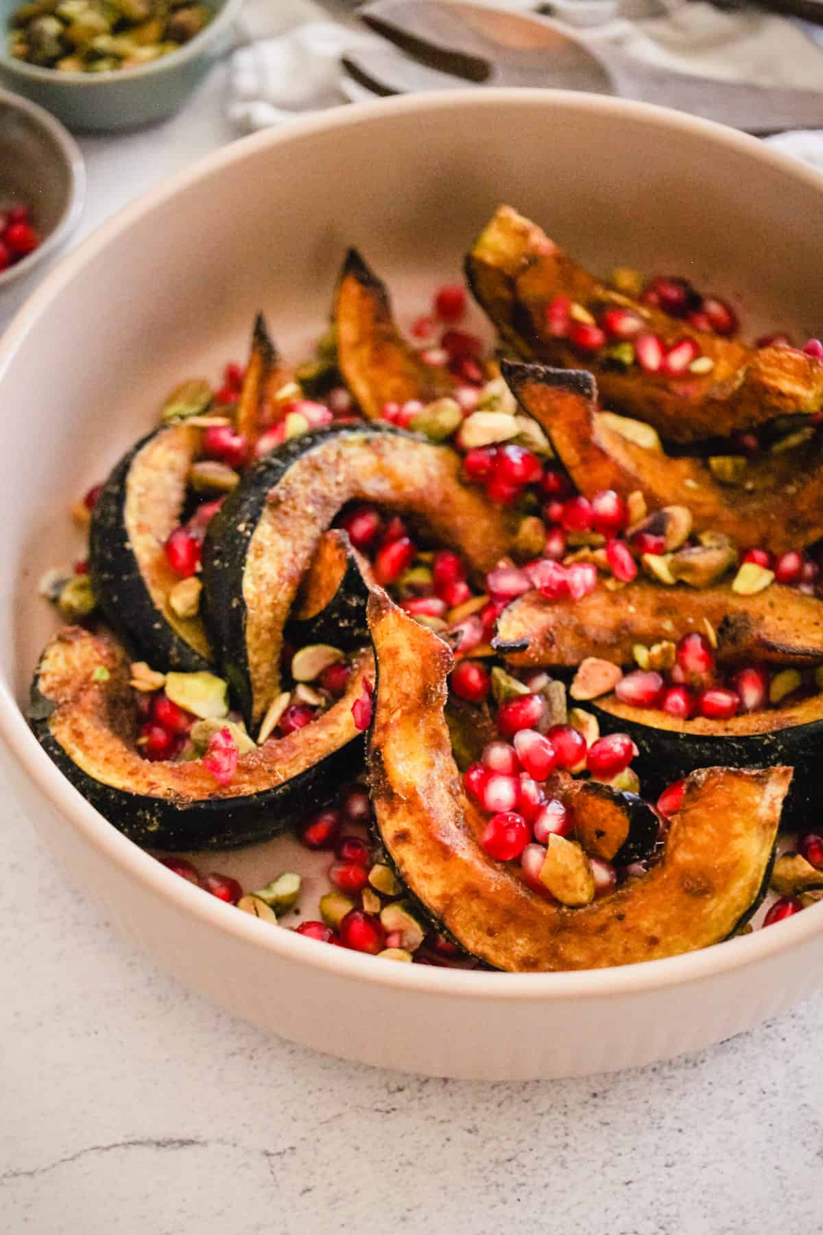 Roasted acorn squash wedges in a serving bowl with pomegranate and pistachios.