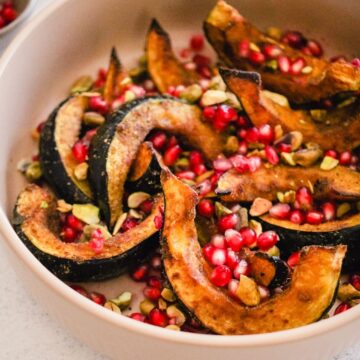Closeup of roasted acorn squash wedges in a serving bowl with pomegranate and pistachios.