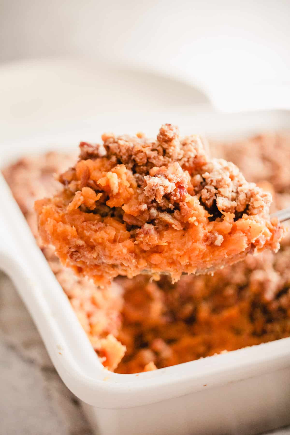 A spoonful of sweet potato casserole above the baking dish.