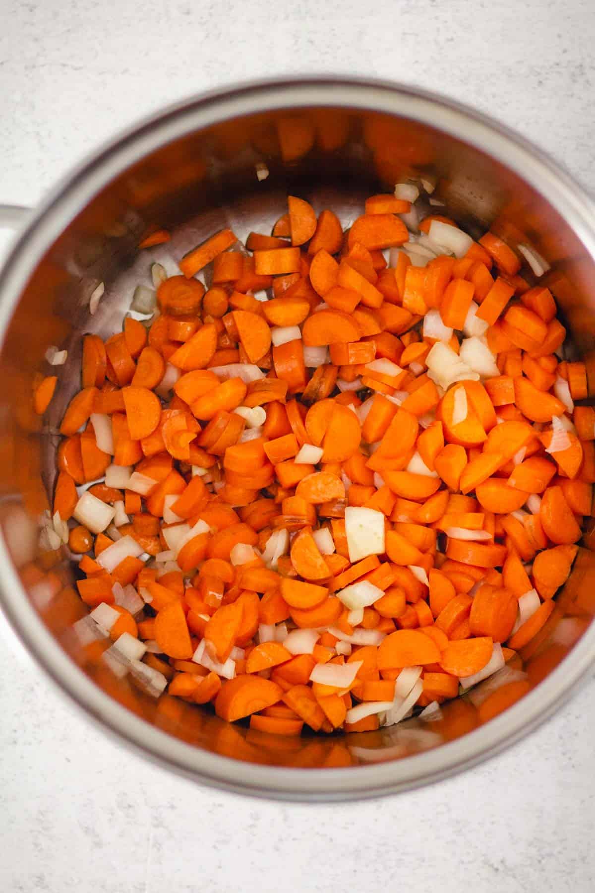 Diced onion and carrots cooking in a large stock pot.