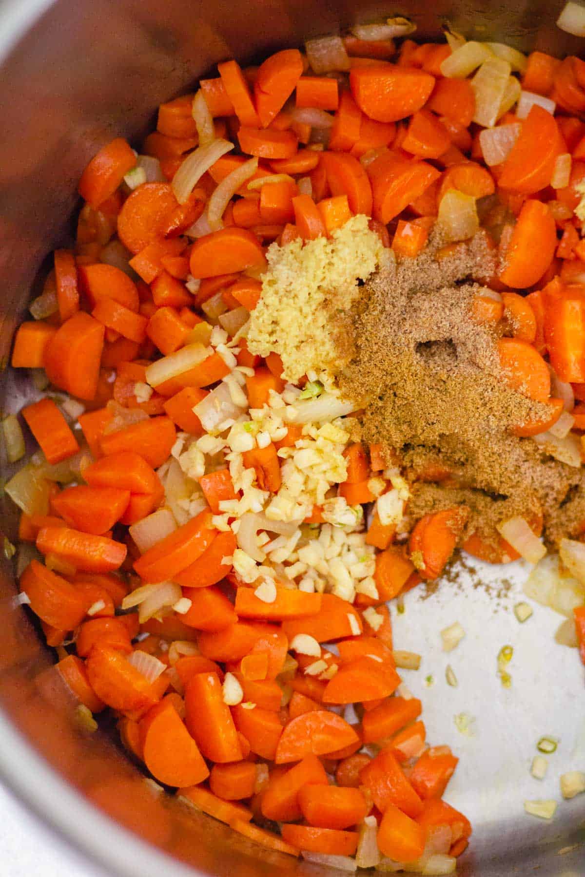 Garlic, ginger, ground spices, carrots, and onion cooking in a large pot.