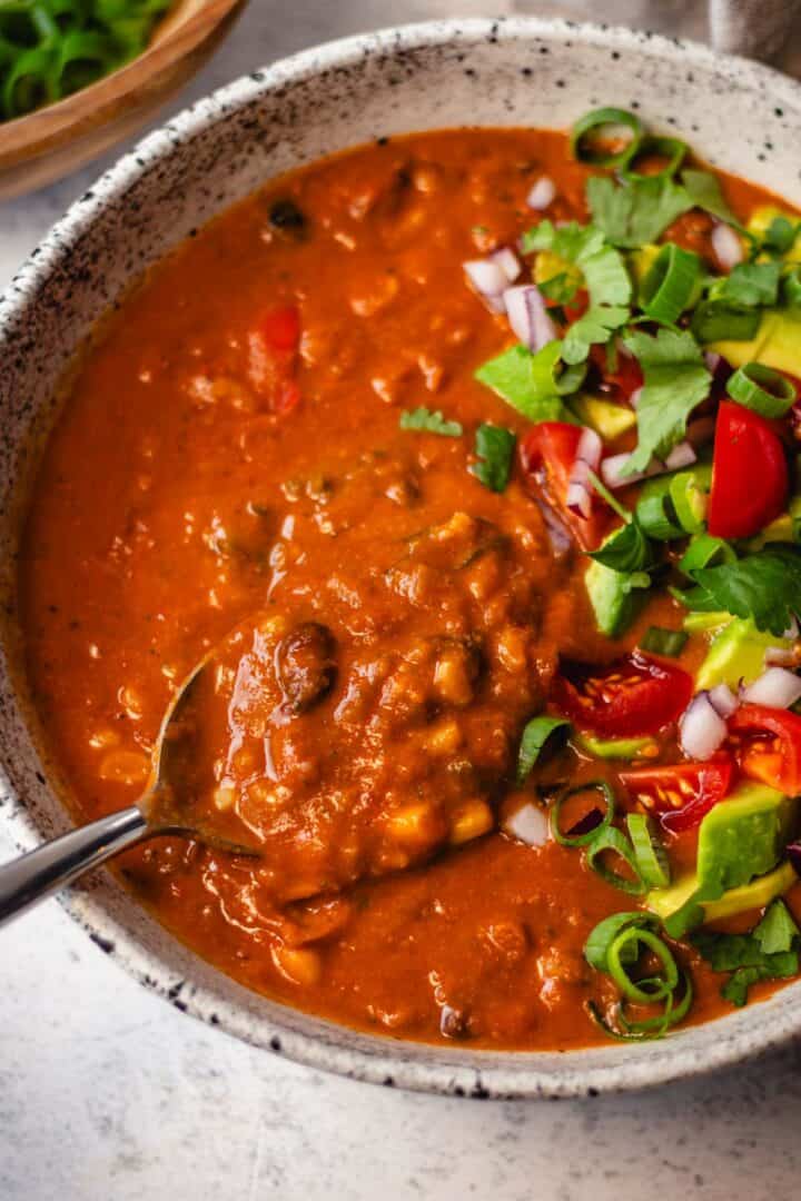 Vegetarian taco soup with beans and rice topped with avocado, onion, tomato, and cilantro.
