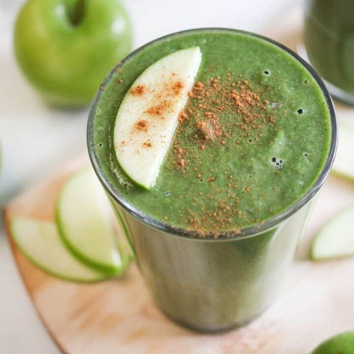 Green smoothie made with lentils in a glass garnished with an apple slice.
