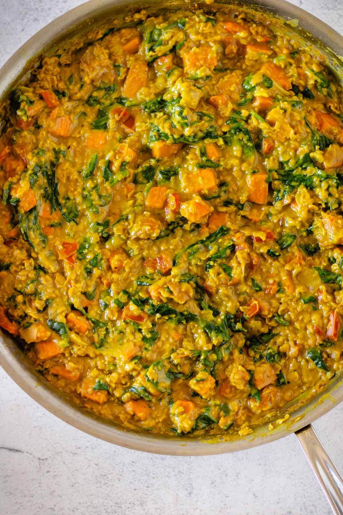 Red lentil curry with sweet potatoes and spinach in a skillet.