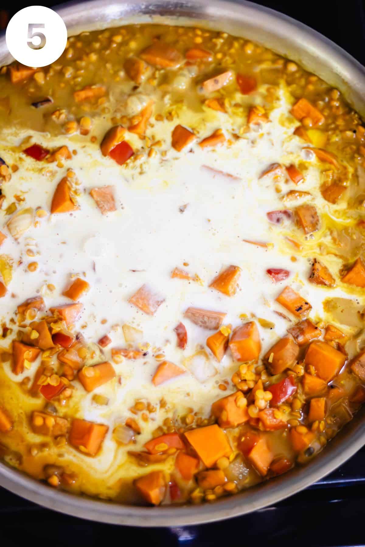 Skillet with lentil and vegetable mixture after a can of coconut milk has been poured on top.