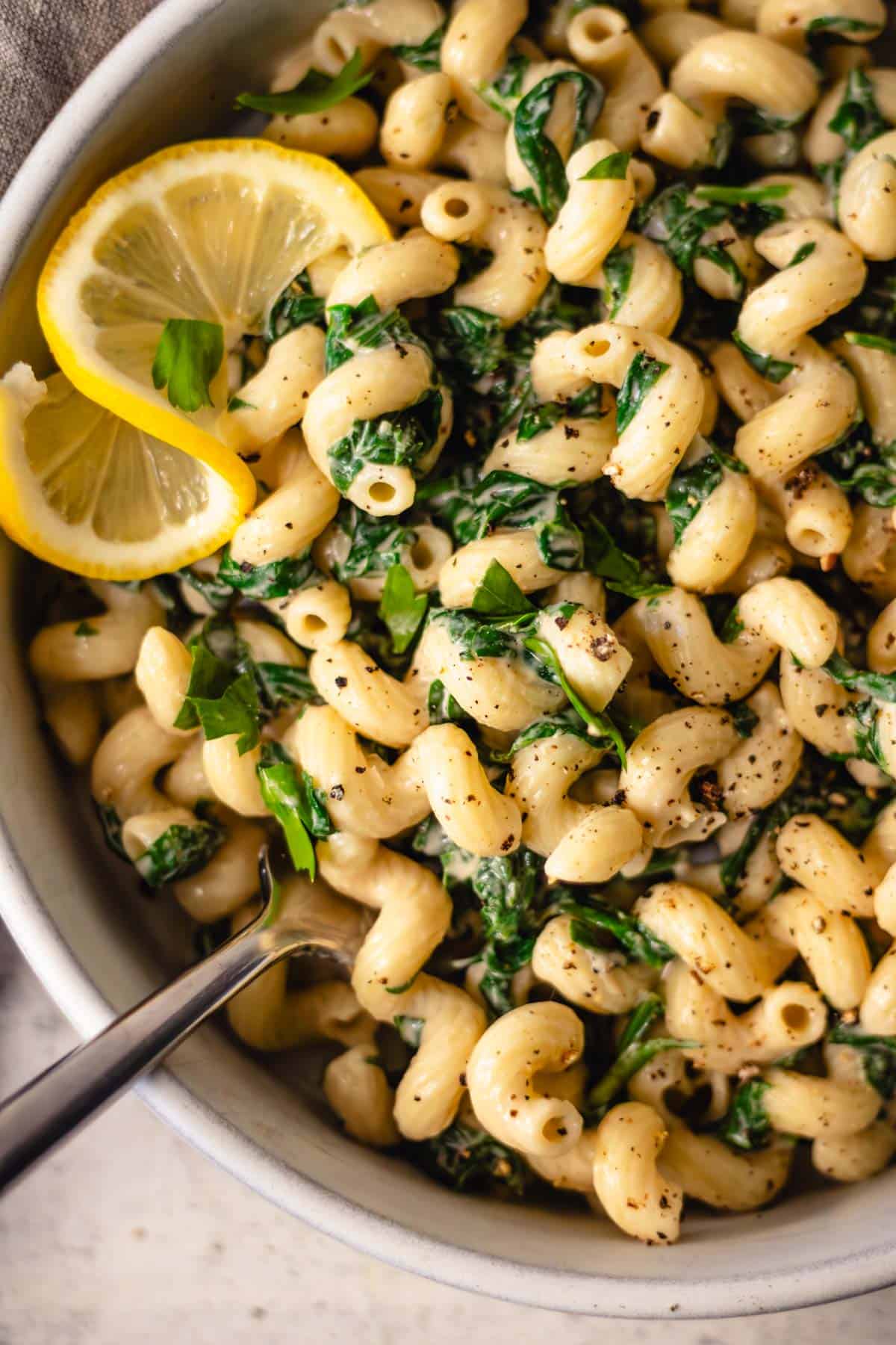 Closeup of creamy tahini pasta in a pasta bowl with spinach garnished with a lemon slice.