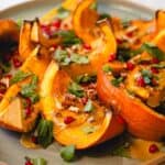 Closeup of oven roasted whole pumpkin sliced into wedges and topped with tahini sauce, pomegranate, nuts, and herbs.
