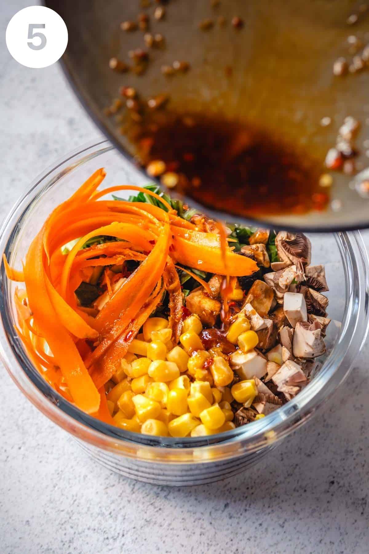 Pouring sesame ginger sauce into a glass bowl of rice noodle soup with vegetables.