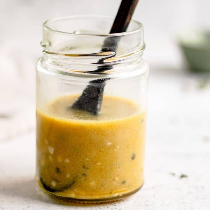 Honey mustard salad dressing in a glass jar with a wood spoon.