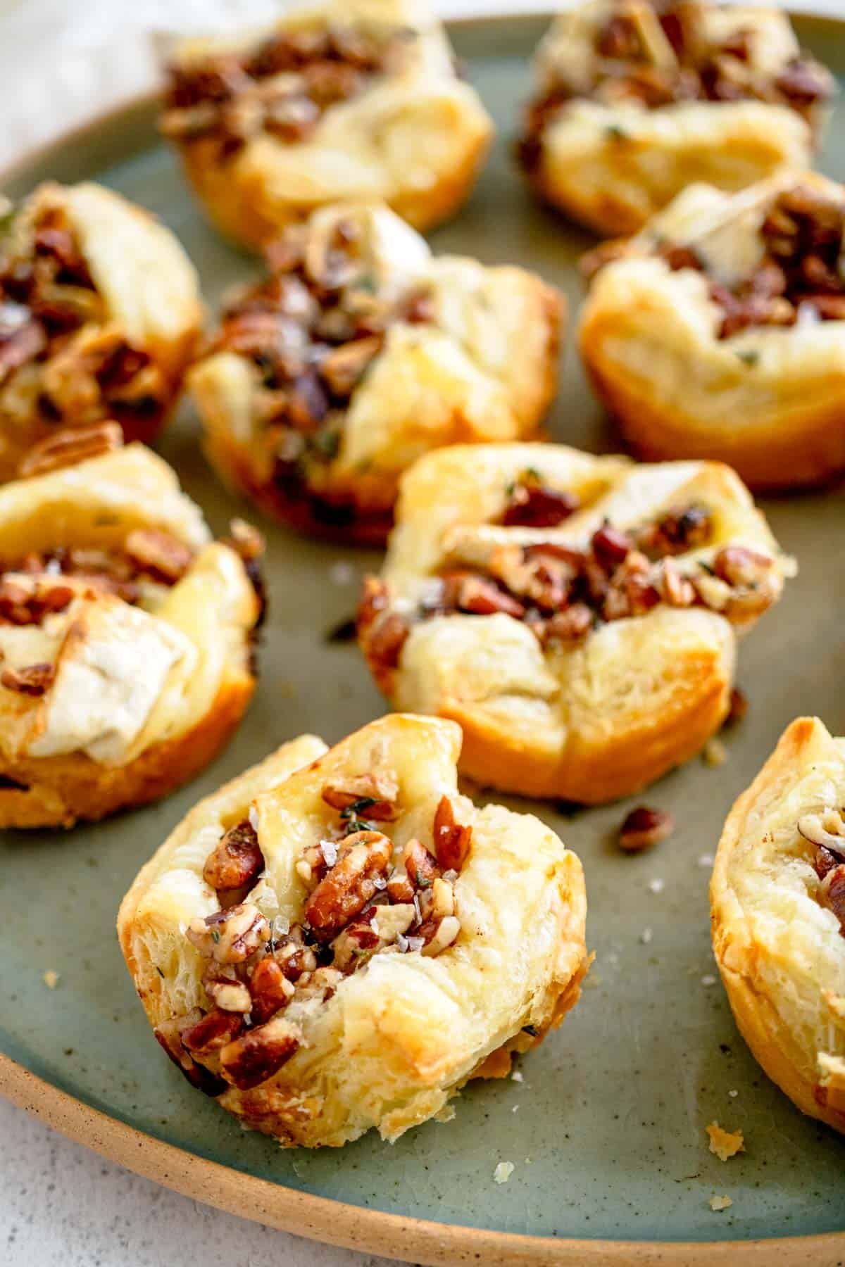 Brie puff pastries topped with pecans and flaky salt on a serving dish.