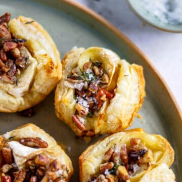 Brie puff pastry appetizer topped with nuts, herbs, and flaky salt.