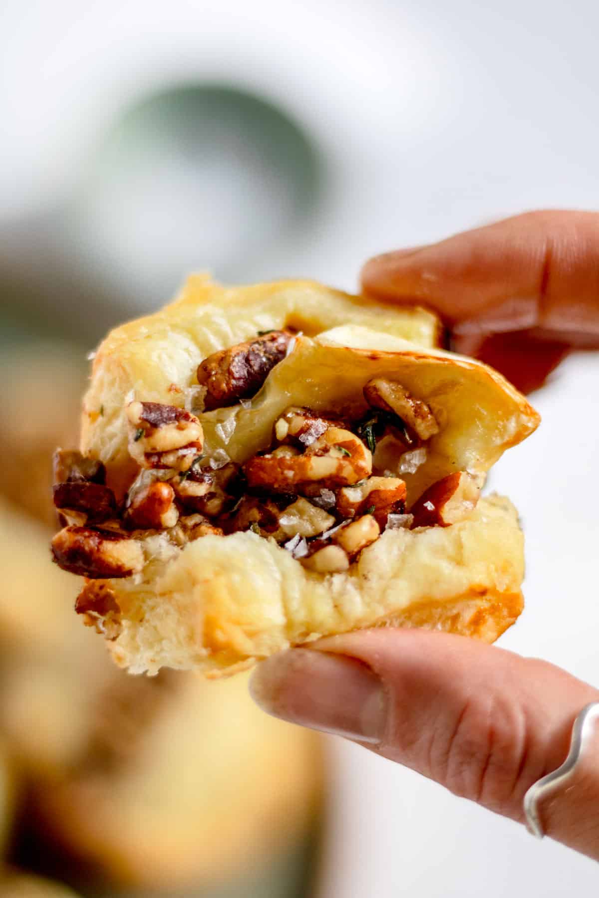 Holding a baked brie puff pastry bite appetizer topped with pecans.