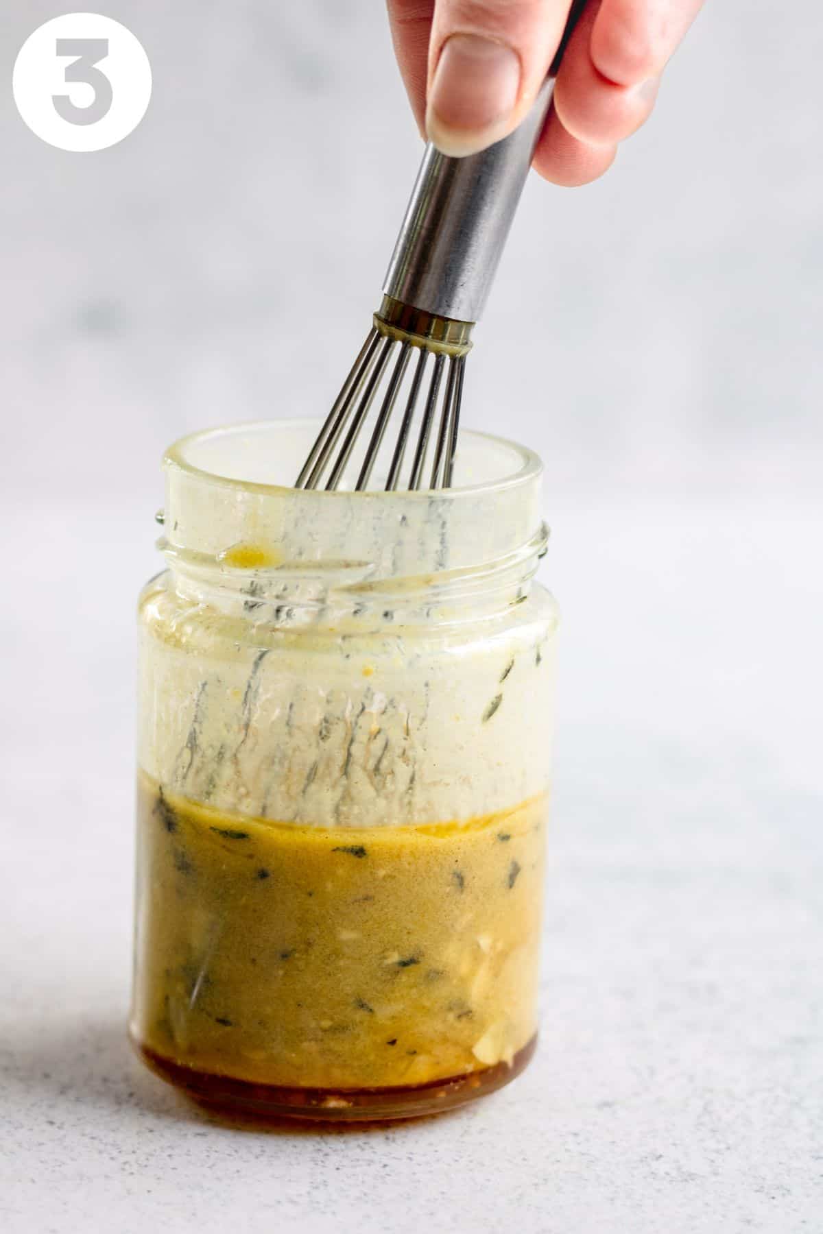 Whisking honey mustard dressing in a glass jar.