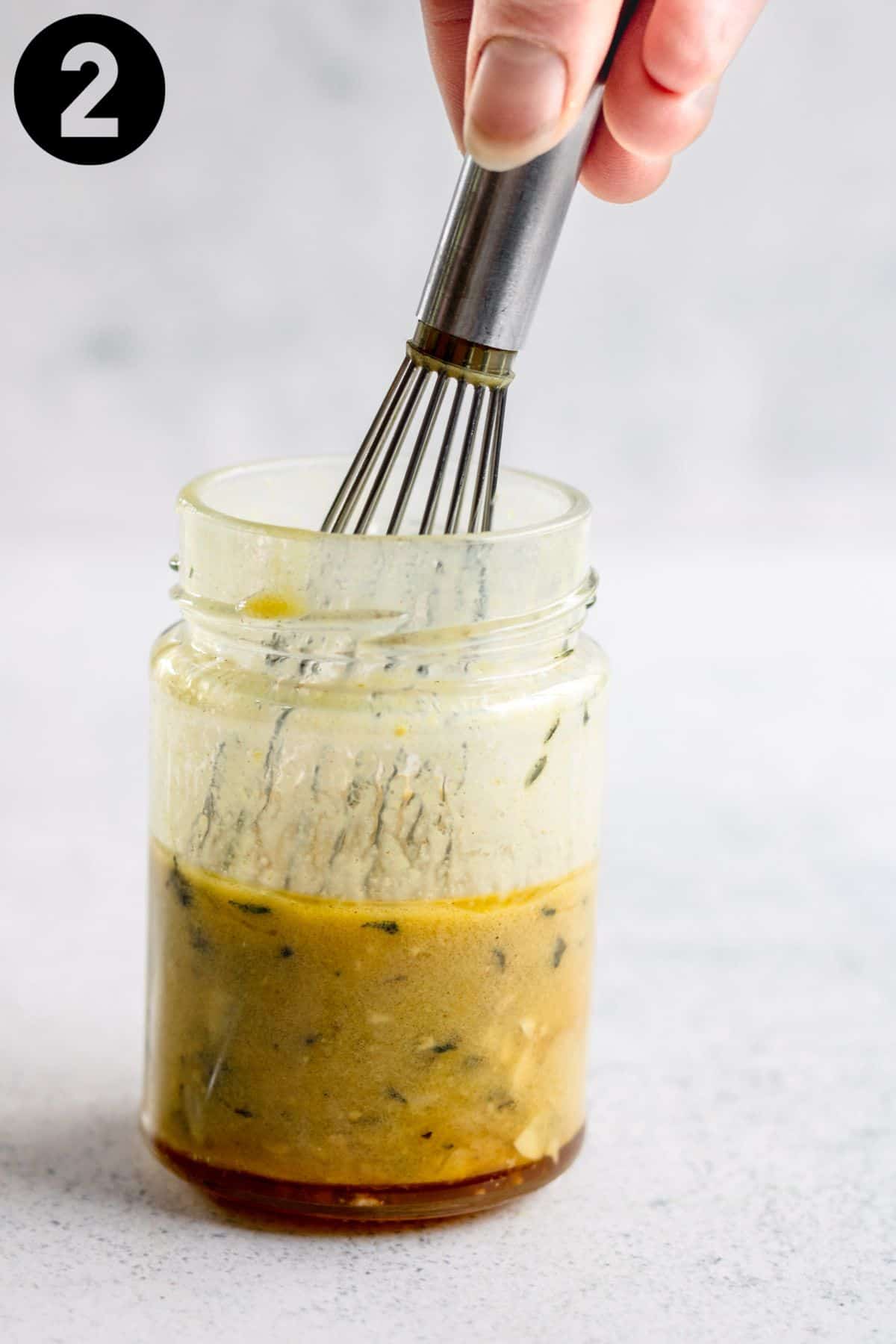 Whisking honey mustard dressing in a glass jar.